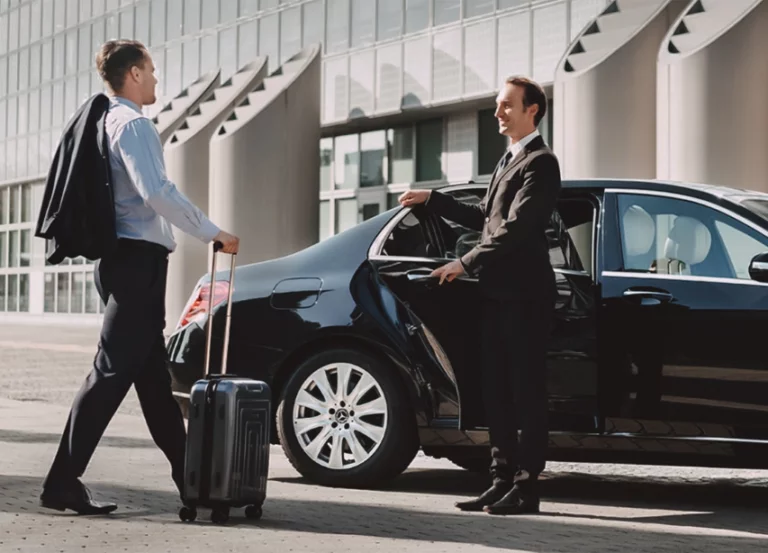 A professional chauffeur holding the door open for a businessman with luggage at an airport.