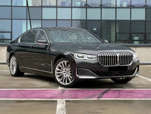 Front-quarter view of a dark grey BMW 740i luxury sedan parked in front of a modern glass building.