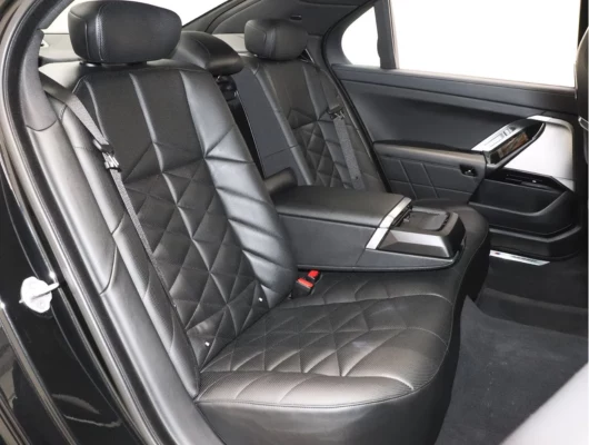 The rear passenger area of a BMW 740i features black leather seats with diamond quilting and a center armrest.