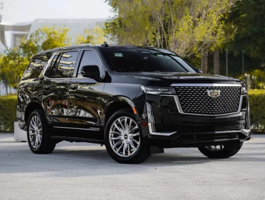 A black Cadillac Escalade luxury SUV parked in a bright outdoor plaza with trees in the background.