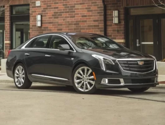 A sleek, black Cadillac XTS sedan parked on a street in front of a brick building.
