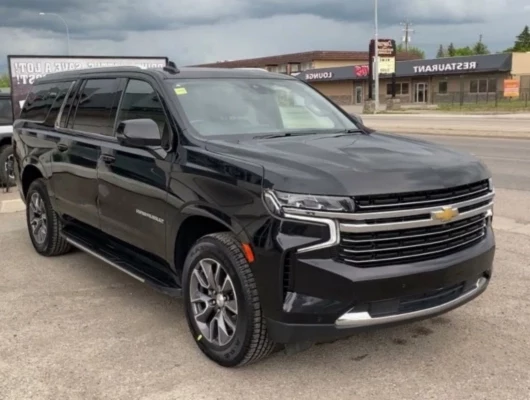 A black Chevrolet Suburban is parked on a gravel lot in front of commercial buildings.