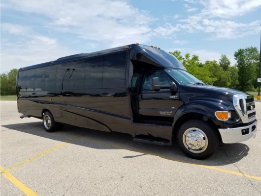 A large black luxury party bus parked in a paved lot under a clear blue sky.