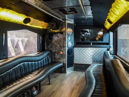 Interior of a luxury party bus featuring neon lighting, leather seating, and a dance floor with a stripper pole.
