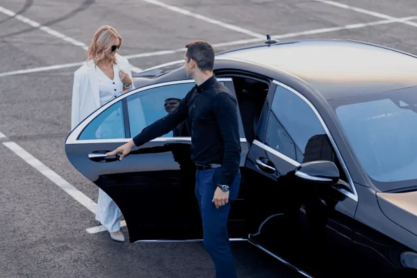 Chauffeur opening the door of a black sedan for a female passenger