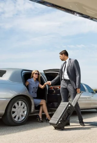 proffessional chauffeur helping a woman get out of a limo at the airport
